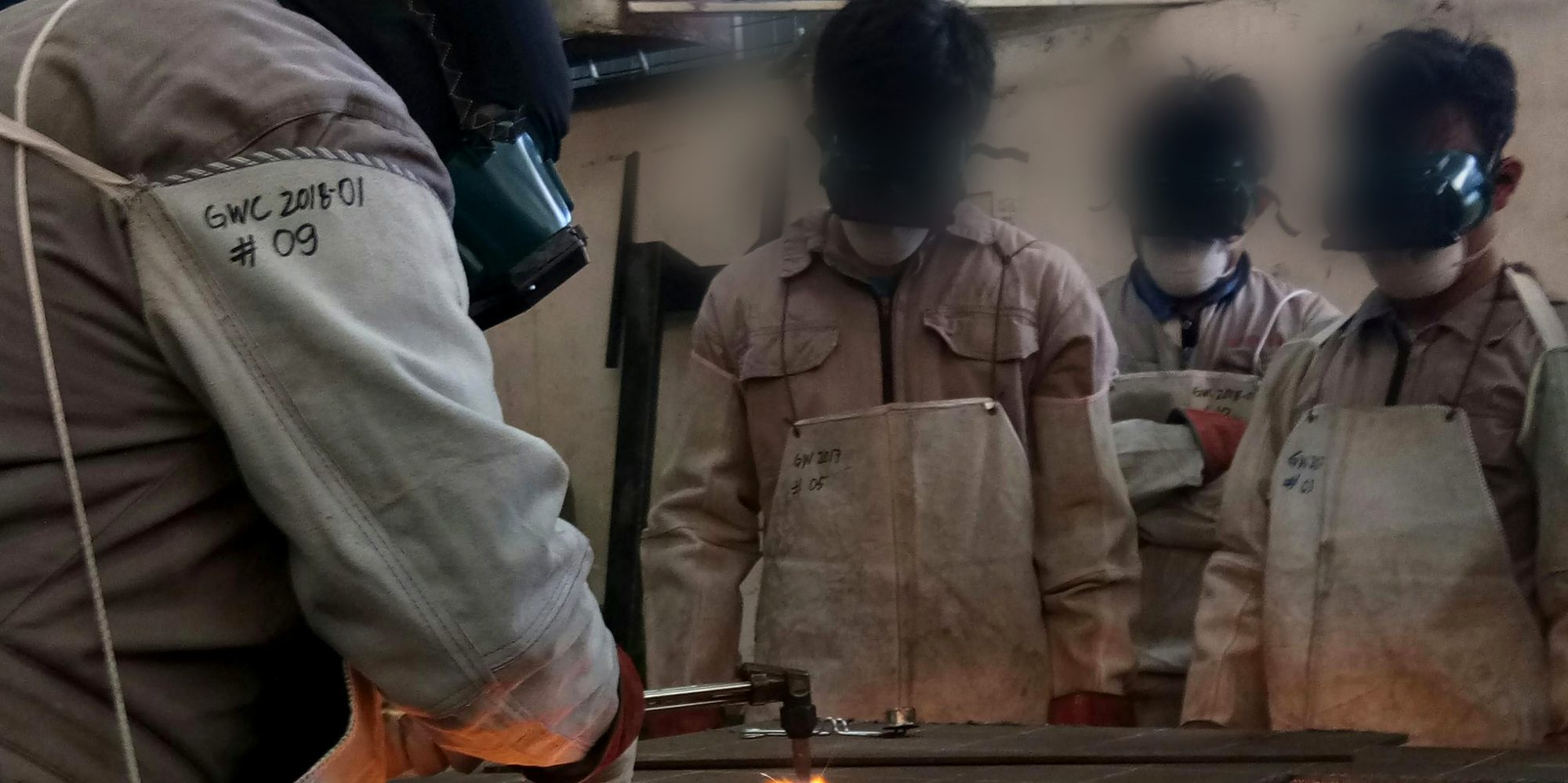 Welding instructor demonstrating oxy-fuel cutting to qualified trainees in industrial training workshop